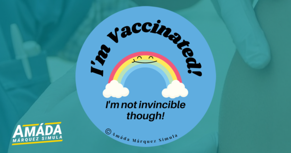 Blue button pin with a smiling rainbow that reads I'm vaccinated! I'm not invincible though!