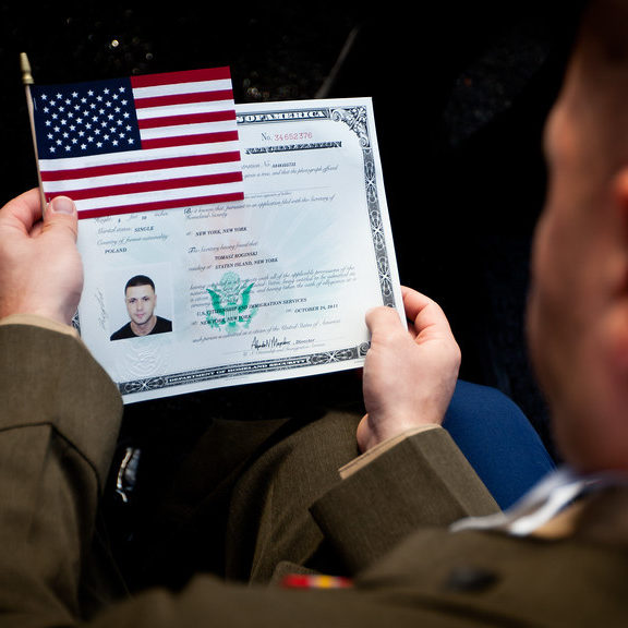 A uniformed person becomes a US citizen, holding an American flag and a naturalization certificate