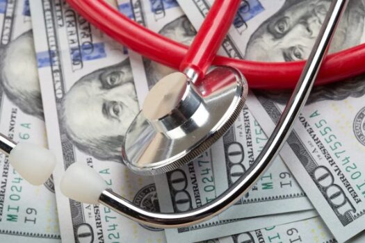 affordable_healthcare A doctor's stethoscope on top of many $100 bills